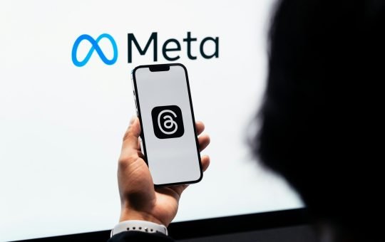 Person holding a phone displaying the Threads social media platform in front of the Meta logo as the company confirms plans to utilise content shared by its adult users in the EU (European Union) on platforms like Instagram and Facebook to train its AI models.